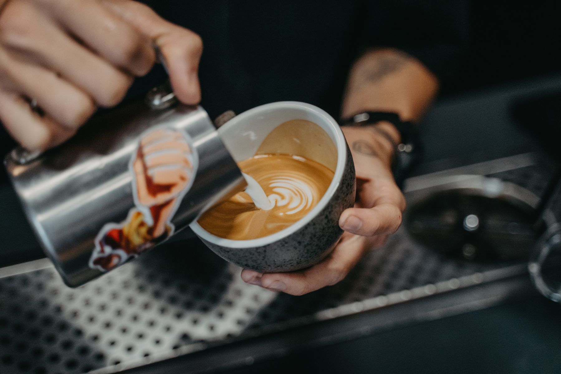 a barista pouring milk to finish a latte